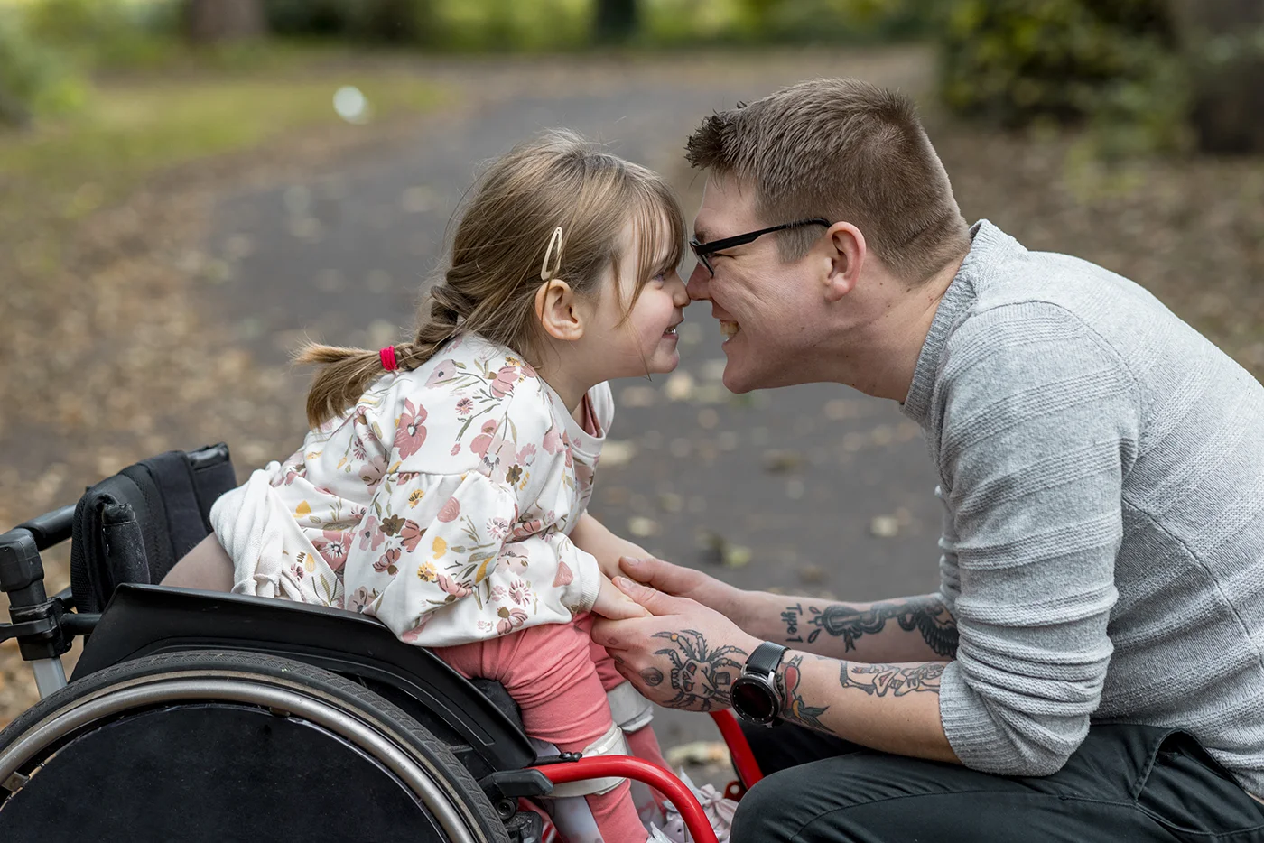 Dad and young daughter smiling at each other. Daughter is a wheelchair user.