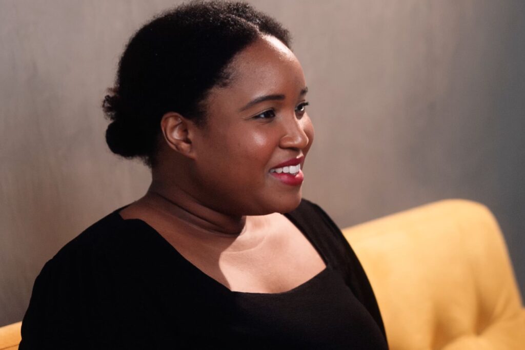 An image of a lady sitting on a sofa, smiling to camera