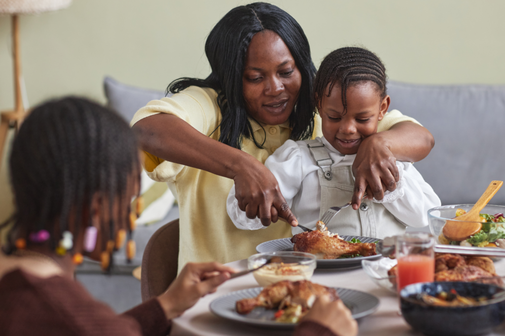 A woman and a toddler at the dinner table, cutting chicken on their plate.