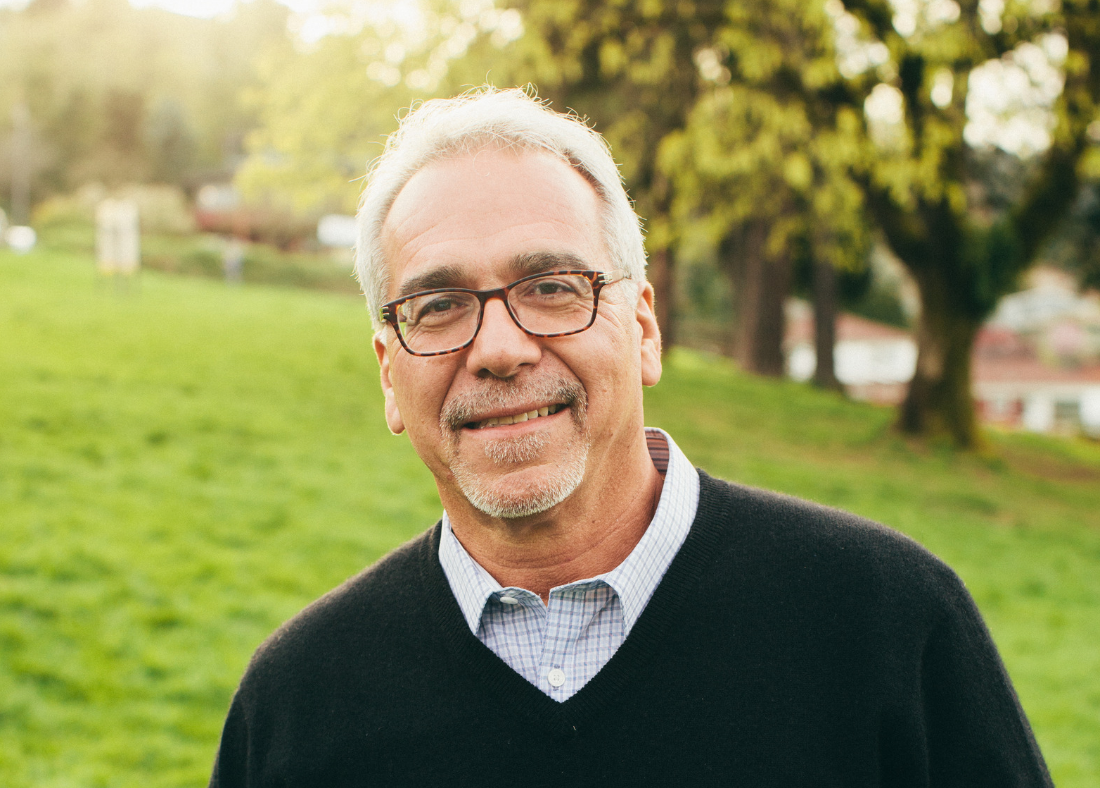 A man standing in the park, smiling to camera